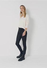 Suéter de pico crema y pantalones ajustados negros, combinados con botas negras de tobillo. Textura suave, diseño minimalista, con sutiles acentos en el hardware.