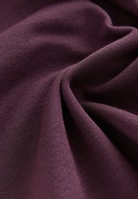 Globoko vijoličen material z gladko teksturo, z rahlim raztezanjem in mehkim sijajem, prepognjen, da prikaže njegov pad in kakovost.