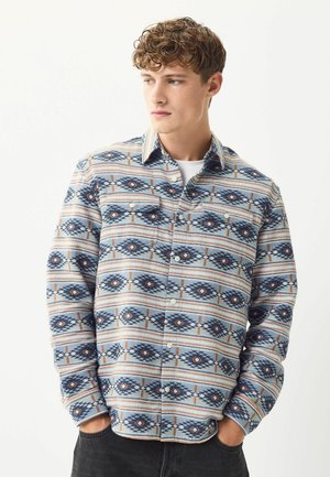 Blue and cream patterned long-sleeve shirt featuring geometric designs, button-down front, and two chest pockets. Soft fabric texture.