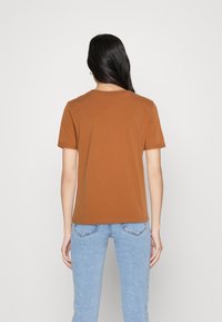 Hnědý bavlněný tričko s krátkým rukávem a kulatým výstřihem. Hladká textura a uvolněný střih, doplněné světle modrými džínami.