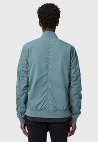 Giacca bomber azzurro chiaro con una texture liscia, polsini e orlo a coste, e una cucitura che scorre verticalmente lungo la schiena.