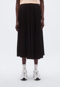 Jupe plissée noire à taille haute avec une texture subtile, portée avec des baskets blanches et des chaussettes côtelées, mettant en valeur une silhouette épurée et moderne.