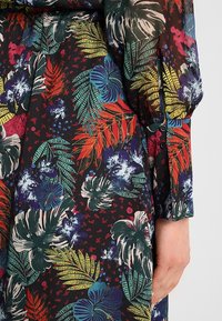 Robe à fleurs avec un fond sombre et des motifs végétaux vibrants en rouge, vert et bleu. Comprend un détail de bouton sur la manche.