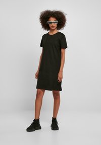 Rochie neagră cu mâneci scurte, croială lejeră, realizată din bumbac moale, până la genunchi, asortată cu adidași negri masivi și ochelari de soare futuristici.