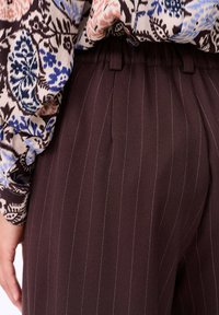 Bruine gestreepte broek van textuurstof, met een aansluitende taille met riemlussen, gecombineerd met een blouse met bloemenpatroon.