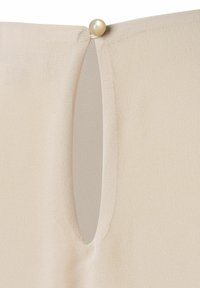 Un tejido beige con una textura suave presenta un corte circular mantenido por un botón decorativo de color crema.