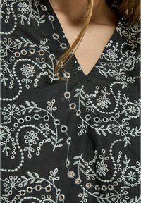 Schwarzes Oberteil aus Stoff mit weißer Blumenstickerei und Ausschnitt-Details. Verfügt über einen V-Ausschnitt und kunstvolle Stickmuster im gesamten Design.
