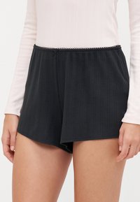 Sorte shorts med en teksturert, ripet design. Har en dekorativ midje med en tynn, svart scalloped kant og liten sløyfe detaj.