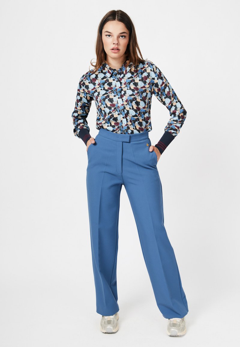 Bluse mit Blumenmuster in Marineblau, Creme und Burgunderrot, mit Knopfverschluss und gerippten Bündchen; hochgeschnittene blaue Hose mit Bundfalten.