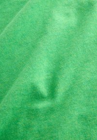 Tissu vert doux avec une texture fine en maille et des plis délicats créant des ombres et des reflets subtils.
