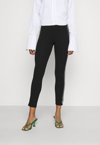 Leggings neri con strisce bianche sui lati e un design aderente. Abbinati a una blusa a righe bianche e sandali con tacco verde e cinturini.