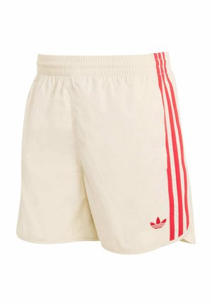 Beige Sportshorts mit elastischem Bund, drei vertikalen roten Streifen an der Seite und einem roten Adidas-Logo nahe dem Saum.