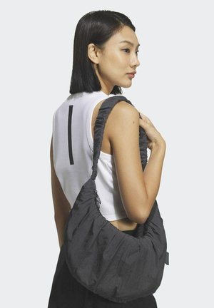 Black fabric handbag with a soft, gathered design. The strap is wide and plush. Worn over the shoulder by a model in a white tank top.