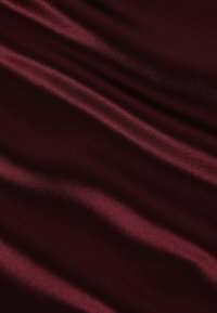 Burgundská sametová tkanina s hladkým, lesklým povrchem, se slabými, vlnitými záhyby a jemnými odrazy světla na celém povrchu.