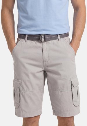 Mann trägt hellgraue Cargo-Shorts mit Seitentaschen und einem grauen Stoffgürtel, die Hände in den Vordertaschen, und ein hellblaues Hemd, das eingesteckt ist.