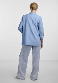 Blazer azzurro chiaro con taglio su misura, maniche lunghe e rever a taglio. Abbinato a pantaloni in denim a lavaggio chiaro, di vestibilità ampia.