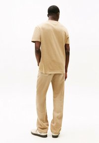 T-shirt beige in cotone casual con maniche corte, abbinato a pantaloni in corduroy beige e scarpe chiare. Vista da dietro.