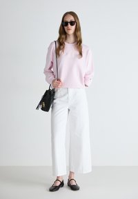 Light pink sweatshirt with embroidered text, white wide-leg pants, black woven handbag, and black flat shoes with a strap detail.