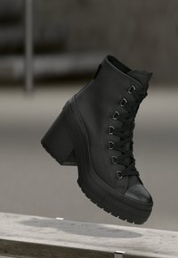 Sorte high-top platform støvler med en struktureret læderoverflade, snøring fortil og kraftig hæl. Har en gummisål med markante mønstre.