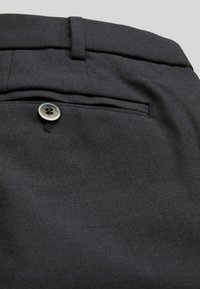 Pantaloni neri con design a vita piatta, texture liscia e una sola tasca posteriore con chiusura a bottone circolare.