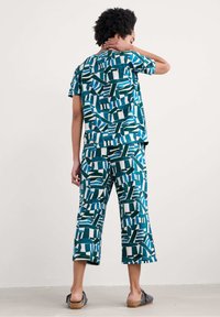 Tvådelad outfit bestående av en kortärmad topp och korta byxor, tillverkad av mjukt tyg med ett blått och vitt abstrakt mönster.