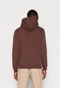 Hnědá mikina s kapucí uvolněného střihu, s žebrovanými manžetami a lemem, vyrobená z měkkého materiálu, s jednoduchým zadním dílem bez ozdob.