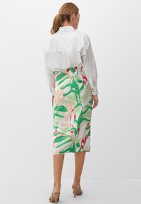 Rok met bloemmotief, van gemiddelde lengte, in groen, roze en witte stof, gecombineerd met een frisse witte overhemd met knopen en beige schoenen.