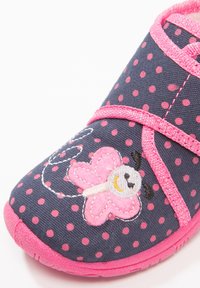 Children's shoe with a navy fabric featuring pink polka dots, pink accents, and an embroidered butterfly design with a smiling face.