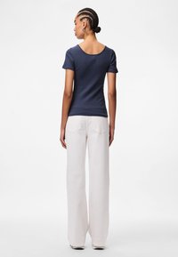 Ναυτικό μπλουζάκι με ραβδωτό σχέδιο, στρογγυλή λαιμόκοψη και κοντά μανίκια, σε συνδυασμό με λευκά παντελόνια με φαρδιά μπατζάκια και πίσω τσέπες.