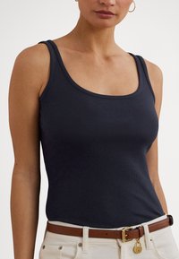 Top de malha azul-marinho com alças largas e decote arredondado. Combinado com um cinto castanho e calças cor de creme. Textura lisa.