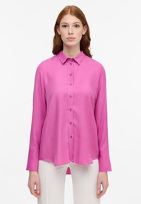 Langærmet bluse i levende pink silke, med krave, knaplukning foran og buet kant. Glat tekstur med knapdetaljer langs fronten.