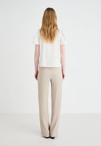 Hvit kortermet bluse med puffede ermer, kombinert med beige høyt liv, plissert, vide bukser. Glatte teksturer og nøytrale farger.