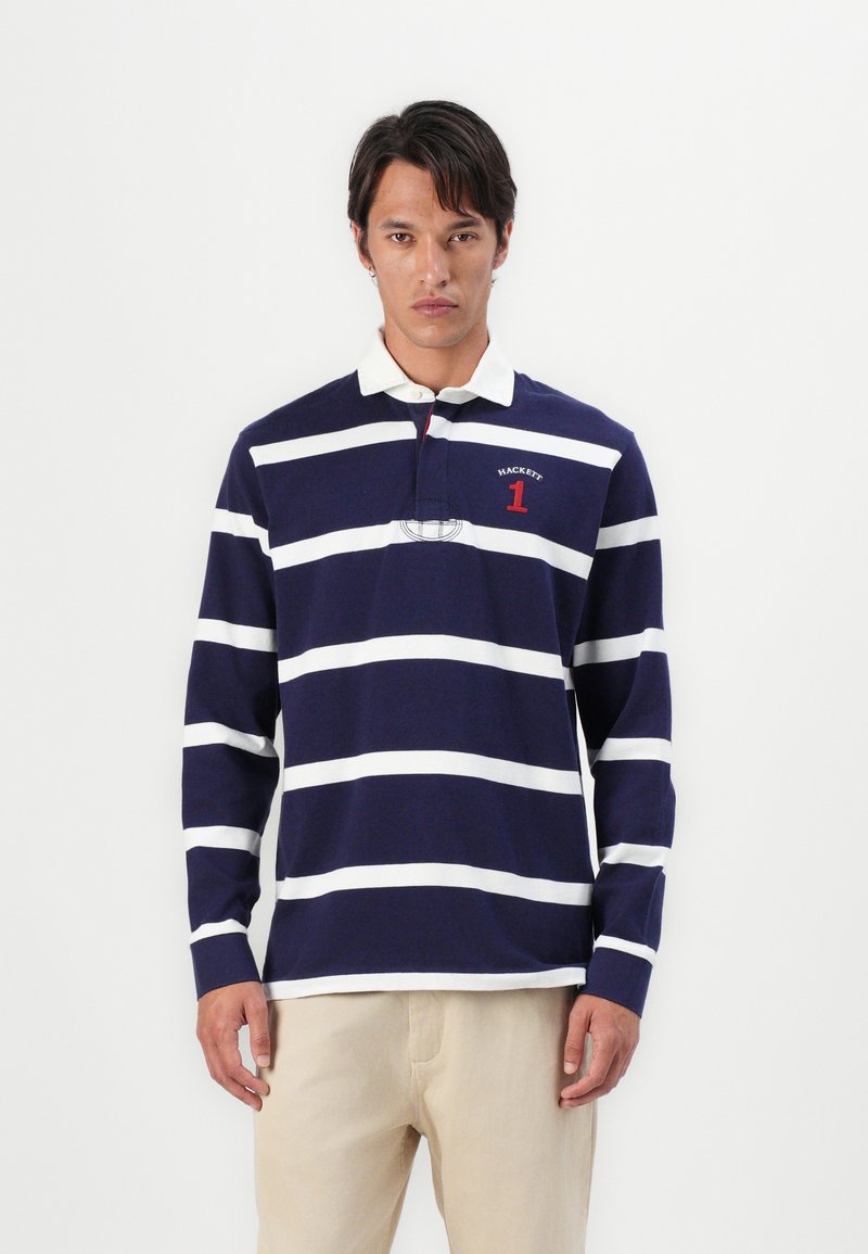 T-shirt de rugby à manches longues bleu marine avec des rayures horizontales blanches, un col, et des détails graphiques rouges. Matière en coton, coupe décontractée.