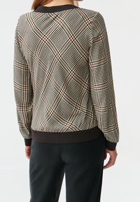 Giubbotto bomber a quadri con colori marrone, nero e crema; polsini e orlo a coste; texture liscia; presenta un collo rotondo.