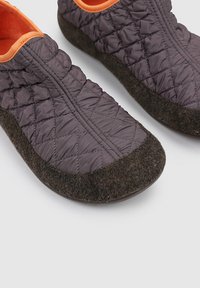 Zapatillas de tela acolchada morada con acentos naranjas y suelas de fieltro marrón oscuro. Punta redondeada y fuelles elásticos para facilitar su uso.