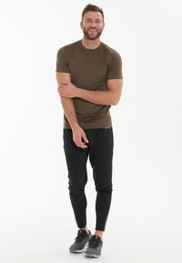 Oliven grøn atletisk skjorte med korte ærmer, parret med sorte tapered jogger bukser med sideløbende striber og atletiske sko.