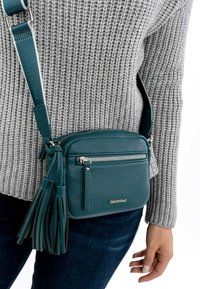 Teal leather crossbody bag with a textured finish, a zippered pocket, and tassel detail. Adjustable strap shows brand name "Emily & Noah."