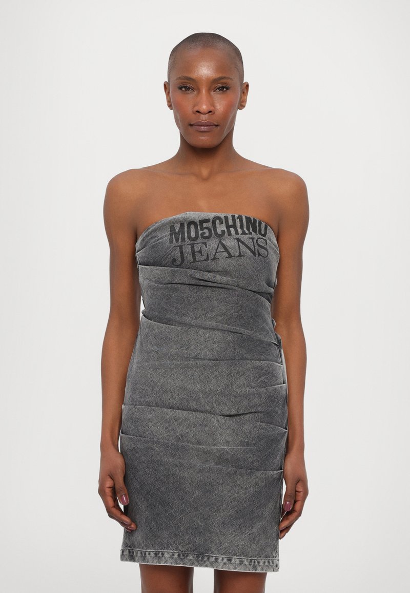 Kratka haljina od sivo traper materijala bez naramenica s naboranom teksturom i Moschino Jeans natpisom na prednjem dijelu. Duljine do sredine natkoljenice s ravnim rubom.
