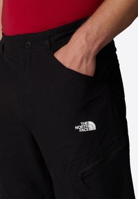Svarta utomhusbyxor med standardpassform, utrustade med en sidofikan och en vit logotyp för "The North Face" på vänster lår.