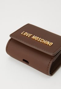 Barna műbőr pénztárca mágneses fedéllel, amelyen arany színű, dombornyomott "LOVE MOSCHINO" felirat található, és egy nyílás a töltőport hozzáféréséhez.