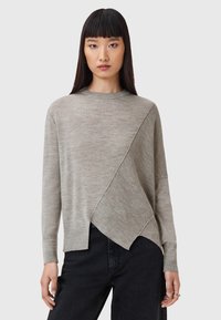 Maglione grigio chiaro con un pannello testurizzato diagonale. Presenta maniche lunghe, un collo a giro e una vestibilità rilassata. Indossato con jeans neri.