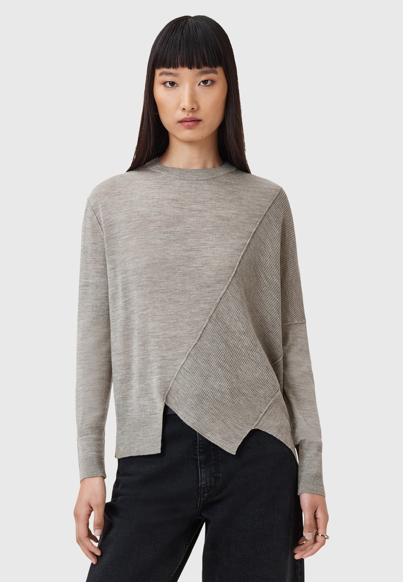 Maglione grigio chiaro con un pannello testurizzato diagonale. Presenta maniche lunghe, un collo a giro e una vestibilità rilassata. Indossato con jeans neri.