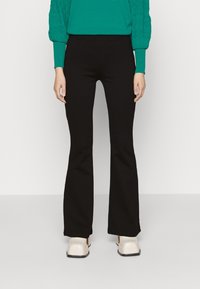 Zwarte flarebroeken met een gladde textuur. Gemaakt met een teal trui en crèmekleurige schoenen. Heeft een aansluitende taille en een klassieke snit.