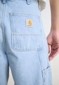 Lys blå denim bukser med en baklomme som har et Carhartt logo-merke. Stoffet er litt falmet med synlige sømdetaljer.
