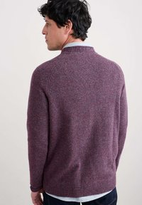 Adīts džemperis bagātīgā bordo krāsā ar sarkaniem un zilajiem pleķiem. Aprīkots ar apaļu kaklu un ribinātu apakšmalu, izgatavots no teksturēta auduma.