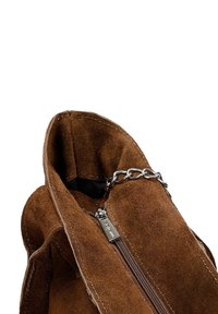 Interno di una borsa in suede marrone con chiusura a zip e accento in catena argentata. Texture morbida con cuciture visibili lungo i bordi.