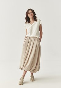 T-shirt bianco a scollo a v, gonna beige fluida a pieghe e sneakers beige. Tessuto morbido e testurizzato con cintura elastica e tasche laterali.
