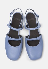 Ljusblå läderskor med öppna sidor och ankelremmar, med en fyrkantig tå. Innersulan har "CAMPER" tryckt i svart.