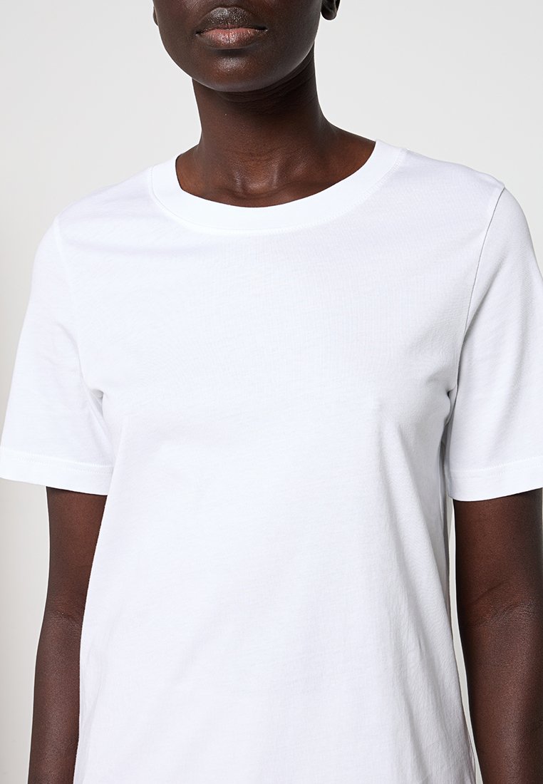 Biała krótka koszulka z krótkim rękawem wykonana z bawełny, z okrągłym dekoltem i gładką teksturą, o luźnym kroju.