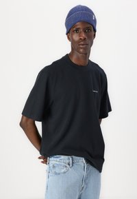 Camiseta de algodón negra con mangas cortas y cuello redondo, combinada con jeans de mezclilla azul claro y un gorro de punto azul.